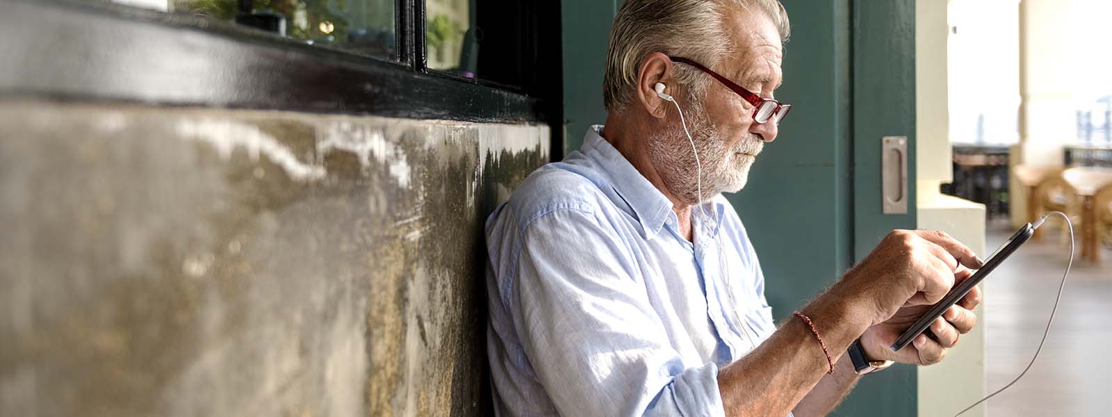 Man sitting on a bench on a sidewalk listening to something in headphones from his phone